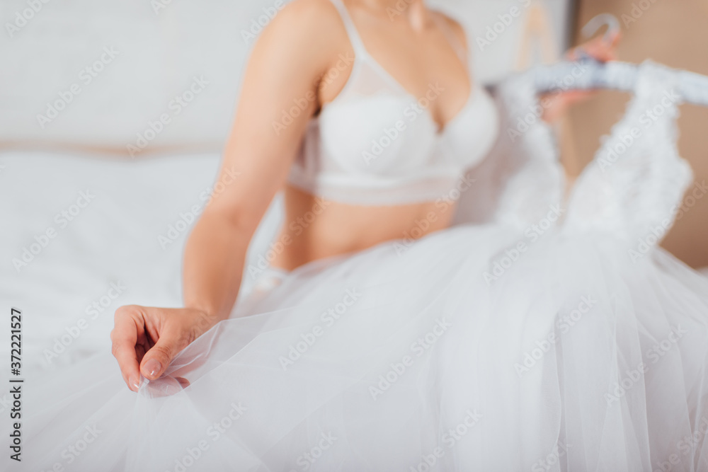 Cropped view of bride in bra touching wedding dress at home Cropped view of bride in bra touching wedding dress at home