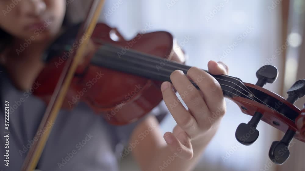 Asian girl playing the violin alone in the room against the curtain window backdrop Asian girl playing the violin alone in the room against the curtain window backdrop