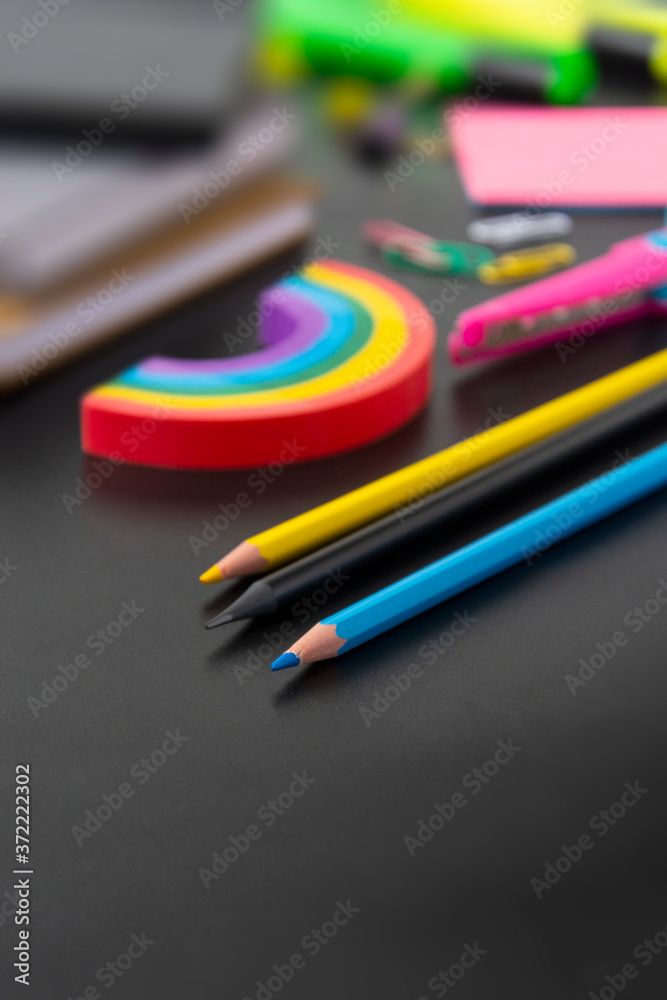 Back to school concept. Colorful pencils, rainbow eraser, notebook, sticky notes and office supplies on black background. Copy space. Back to school concept. Colorful pencils, rainbow eraser, notebook, sticky notes and office supplies on black background. Copy space.