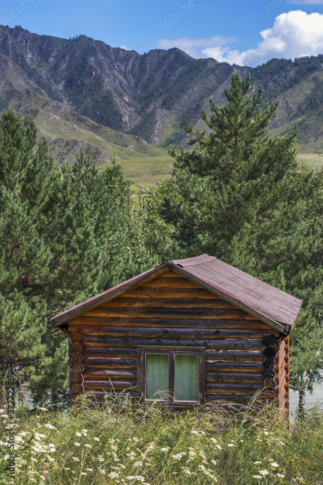 A small log house for tourists stands against the backdrop of the mountain slopes. Travel through the Altai Republic in Russia in the summer months.
