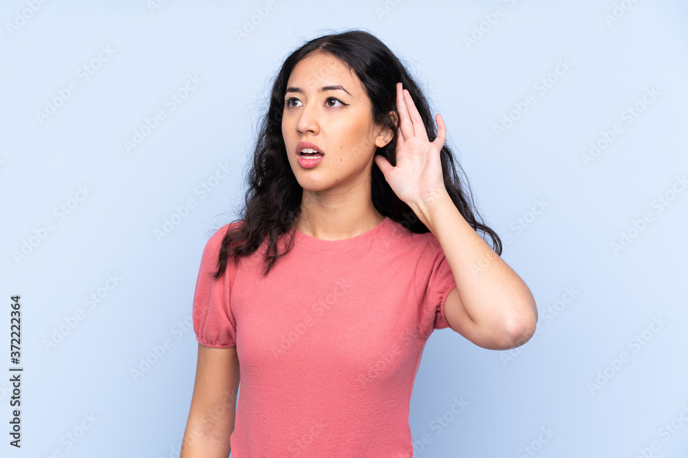 Mixed race woman wearing a sweater over isolated blue background listening something Mixed race woman wearing a sweater over isolated blue background listening something
