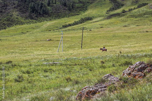 A mountain dweller rides a horse along the hills along the power lines. Travel the Altai Republic of Russia during the summer months.