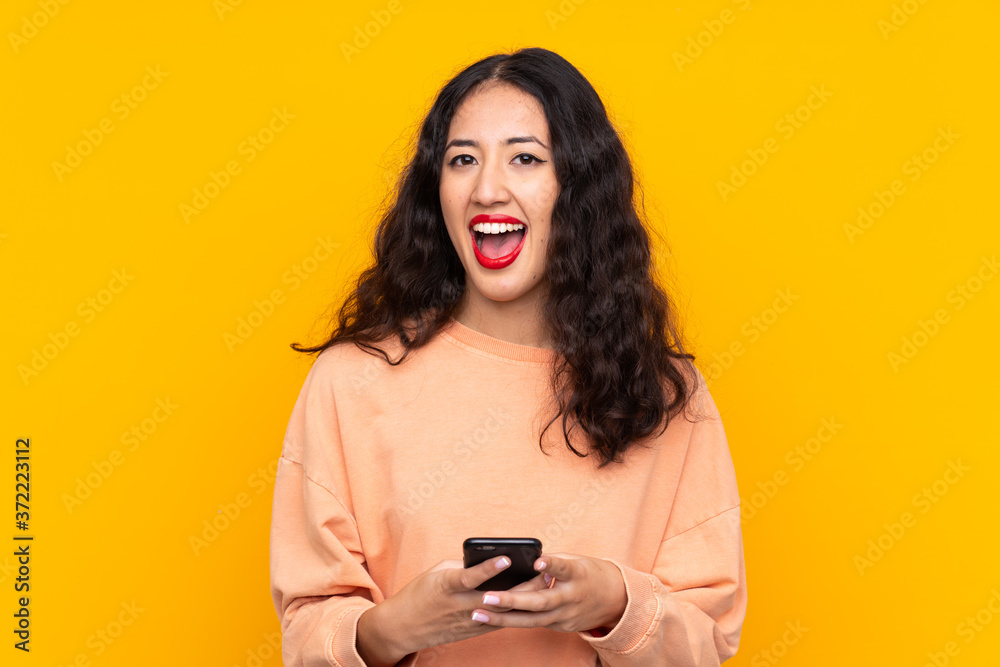 Spanish Chinese woman over isolated yellow background surprised and sending a message Spanish Chinese woman over isolated yellow background surprised and sending a message