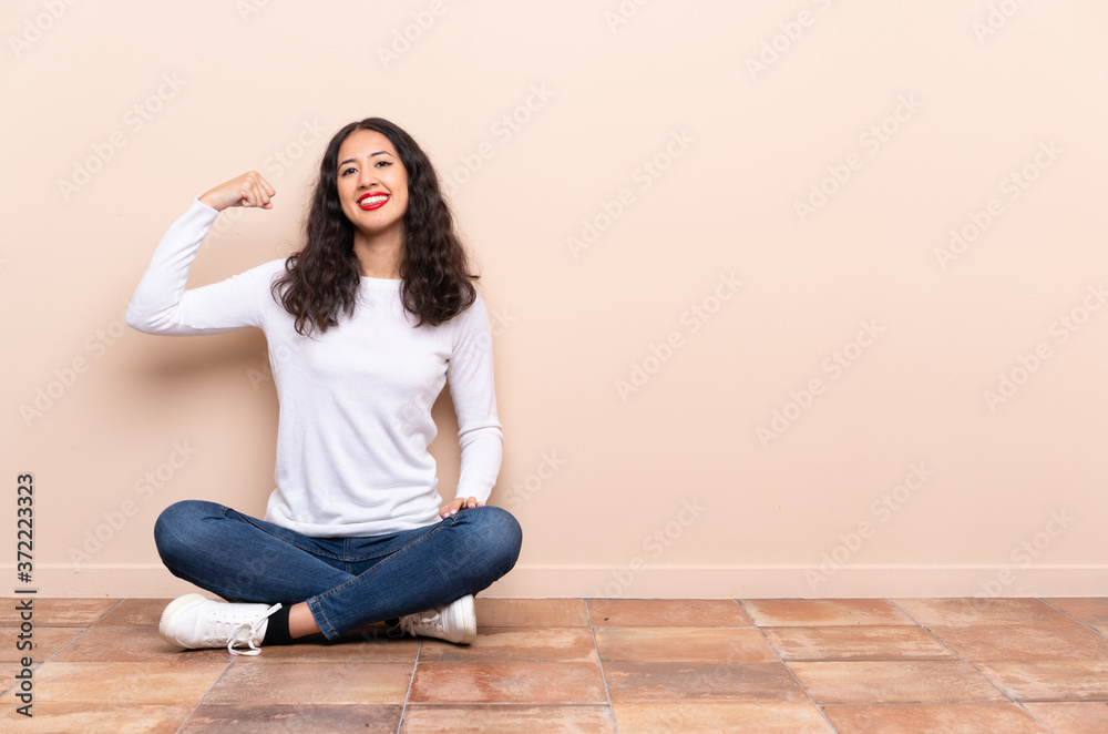 Young woman sitting on the floor doing strong gesture Young woman sitting on the floor doing strong gesture