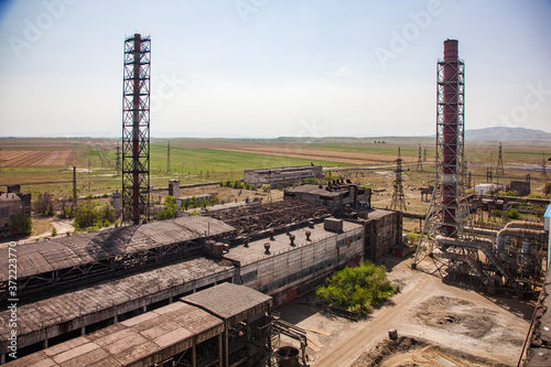 Abandoned metallurgy factory buildings and rusted factory chimneys. On the blue sky, steppe and mountain background. Taraz city, Kazakhstan
