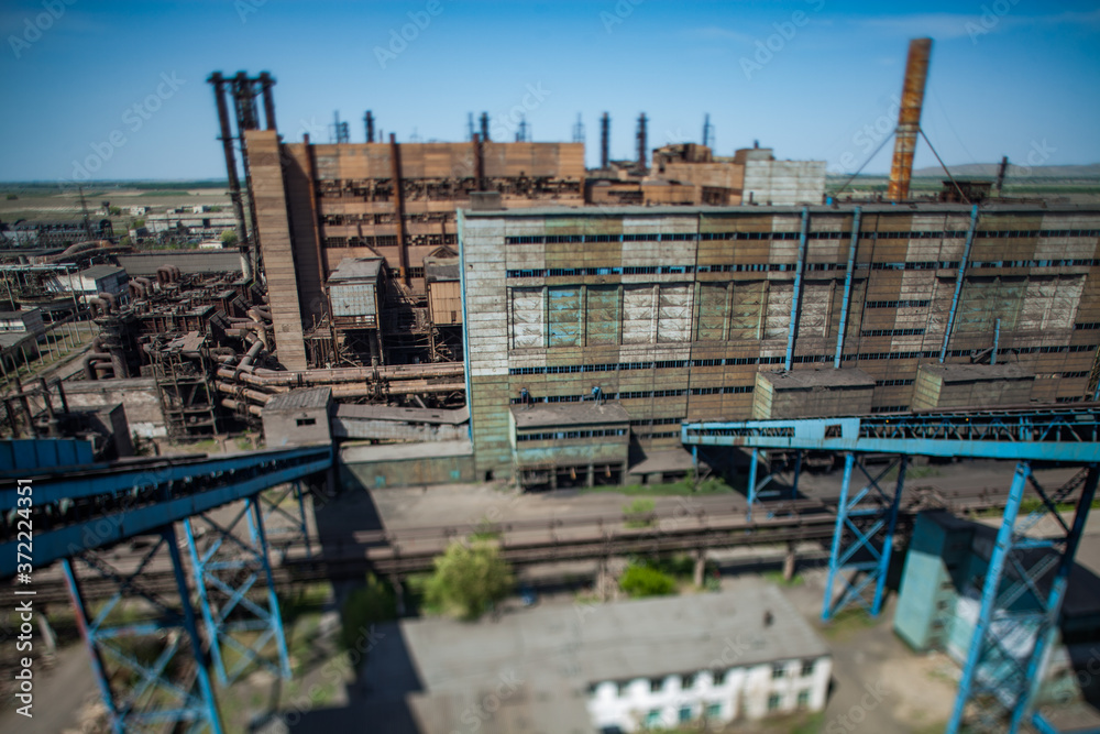 Abandoned soviet metallurgy plant buildings and rusted chimneys on blue sky. Aerial view with tilt-shift effect lens. Partially blurred. Taraz city