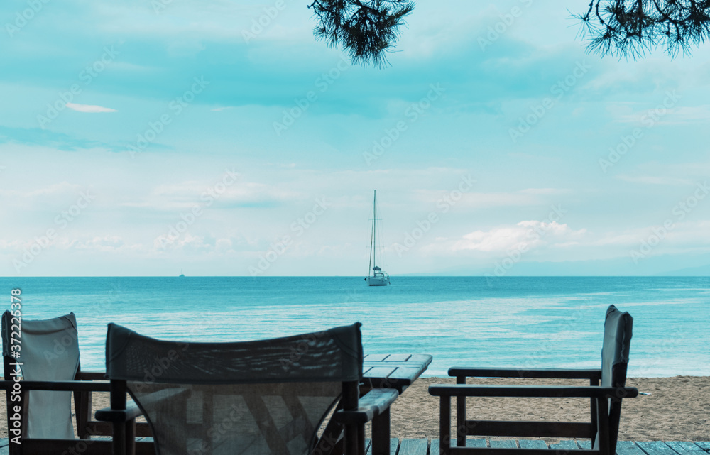 chairs on a tropical beach with a calm sea and a sailing boat in the background