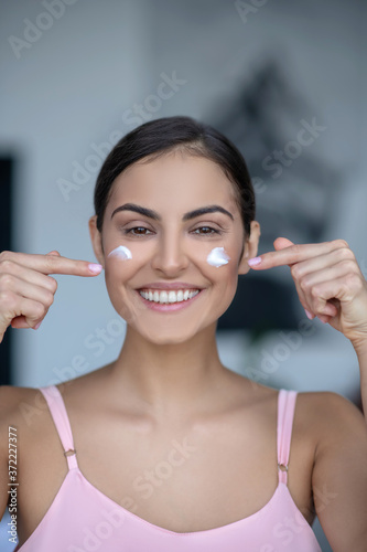Woman in pink lingerie applying cream on her face