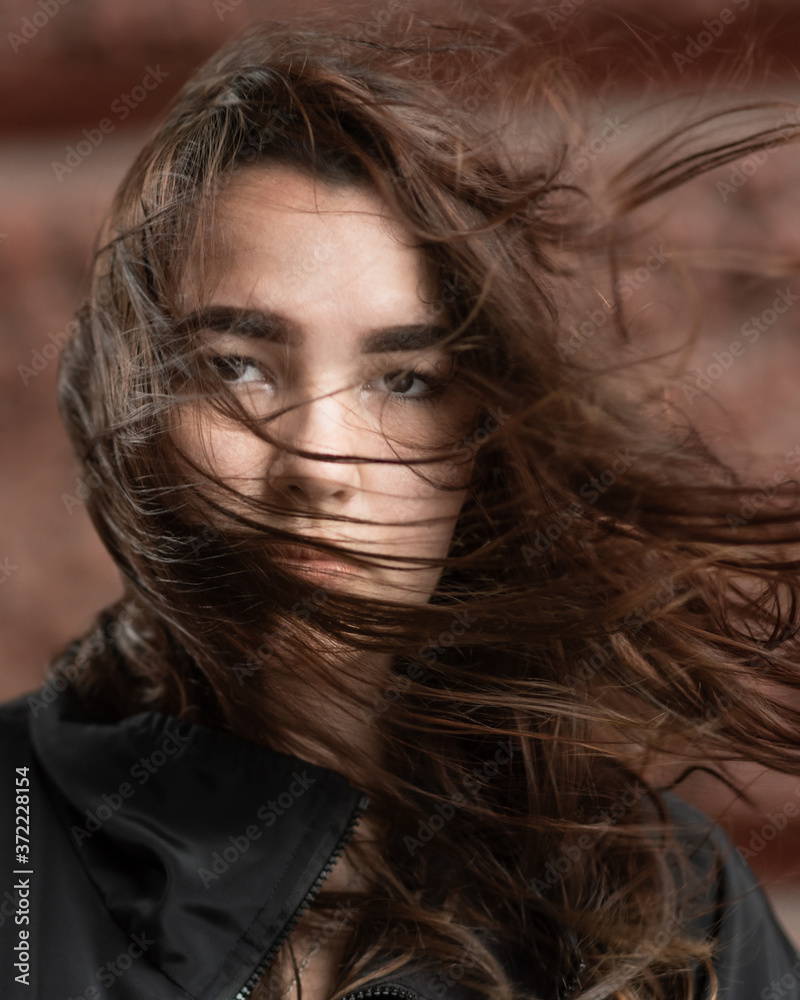 Young woman with disheveled hair by the wind looks at the camera Young woman with disheveled hair by the wind looks at the camera