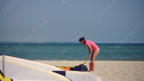 Middle-aged woman pumping up up a kitesurfing kite at the beach on summer vacation in hot sunshine with ocean backdrop
