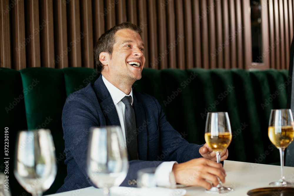 Handsome businessman dressed in the suit drinking wine. Businessman and businesswoman enjoying in the restaurant.