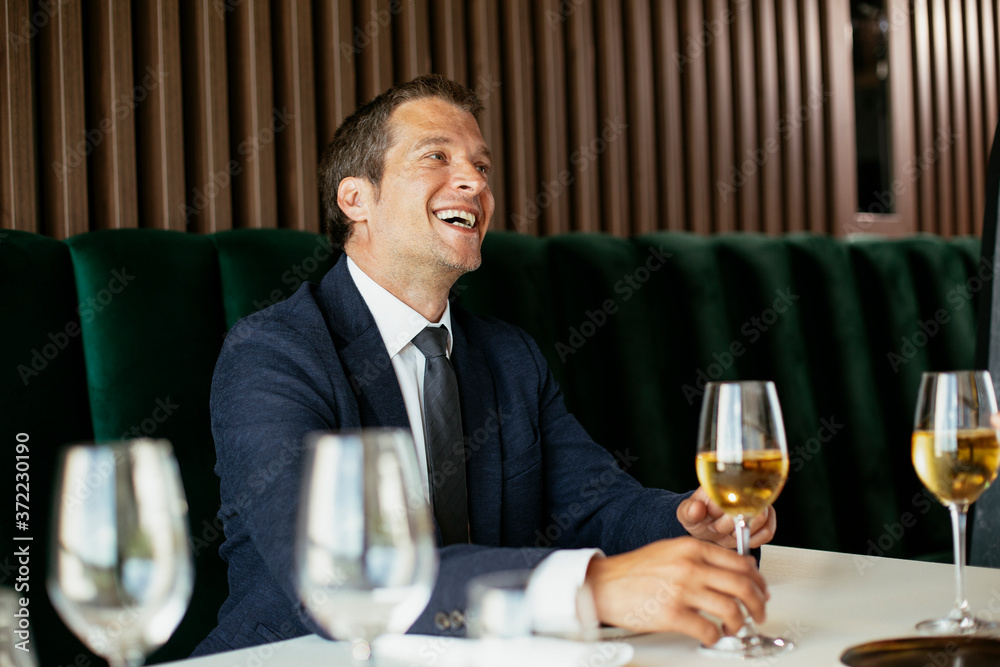 Handsome businessman dressed in the suit drinking wine. Businessman and businesswoman enjoying in the restaurant. Handsome businessman dressed in the suit drinking wine. Businessman and businesswoman enjoying in the restaurant.