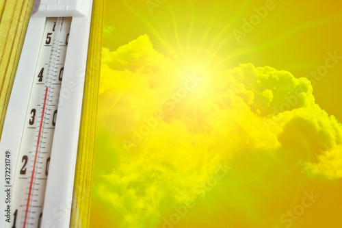 Heat wave - the concept of global warming. Summer heat. Thermometer +39°C against a hot yellow sky and sun.