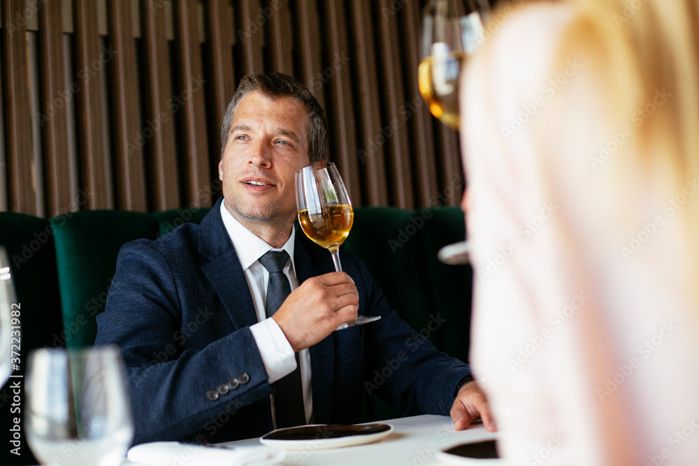 Handsome businessman dressed in the suit drinking wine. Businessman and businesswoman enjoying in the restaurant.