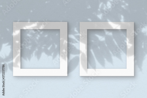 Two square sheet of white textured paper on the blue wall background. Mockup with an overlay of plant shadows. Natural light casts shadows from the leaves of an exotic plant. Flat lay, top view