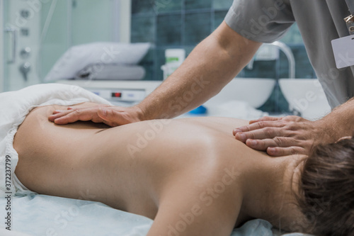 Masseur is doing massage of back of woman lying in beauty salon. Professional is massaging and touching skin of female client, using traditional techniques. Specialist works with body of patient