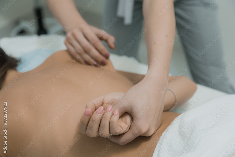 Young woman having massage in cosmetology clinic. Close-up of woman relaxing during back massage lying on massage table. Masseur gives a therapeutic massage to a beautiful woman.