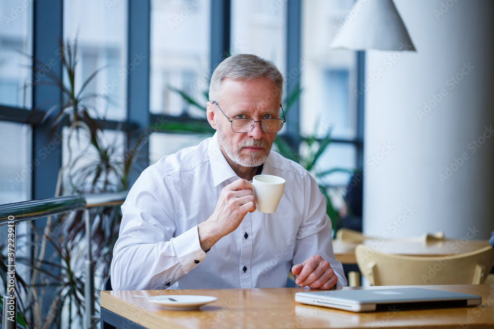 Adult man in glasses manager businessman worked successfully and at the end of the day drinks coffee without a jacket Adult man in glasses manager businessman worked successfully and at the end of the day drinks coffee without a jacket