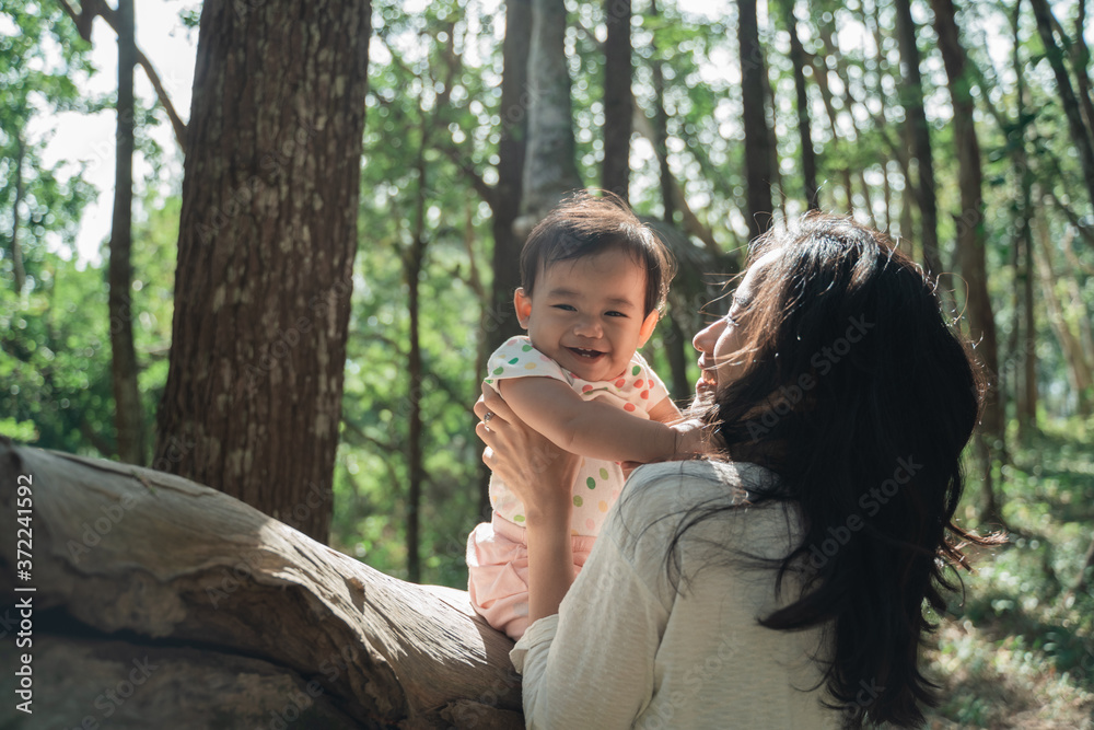 The baby girl is laughing happily and her mother plays together against the background of the trees as they enjoy their vacation in the park The baby girl is laughing happily and her mother plays together against the background of the trees as they enjoy their vacation in the park