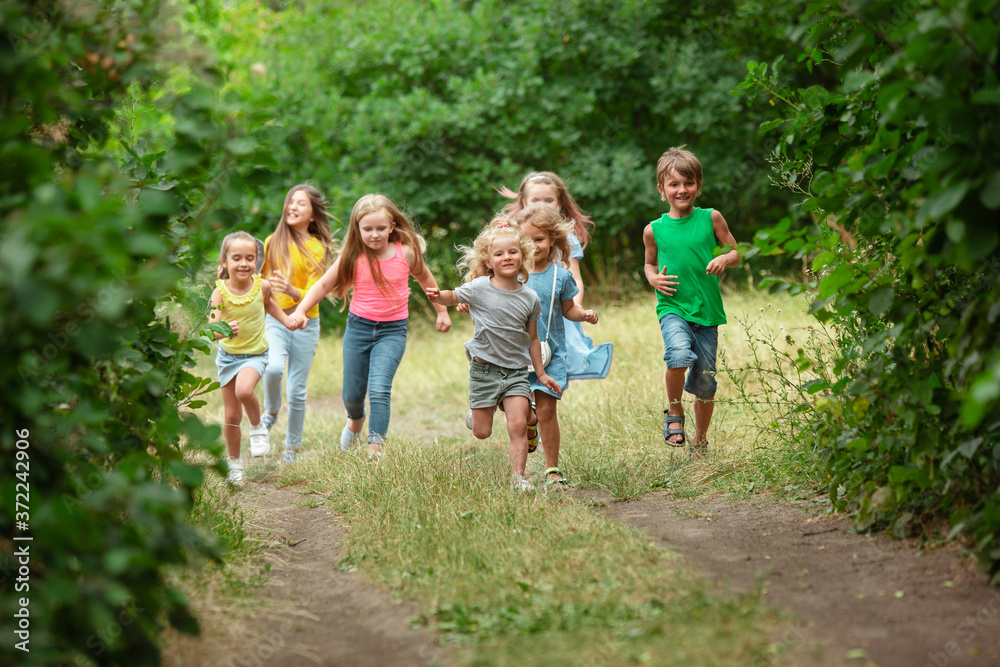 Happiness. Kids, children running on green forest. Cheerful and happy boys and girs playing, laughting, running through green blooming meadow. Childhood and summertime, sincere emotions concept.