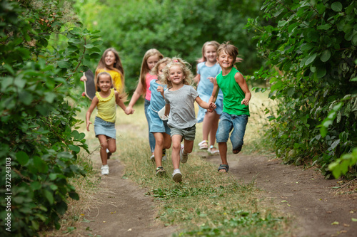 Happiness. Kids, children running on green forest. Cheerful and happy boys and girs playing, laughting, running through green blooming meadow. Childhood and summertime, sincere emotions concept.