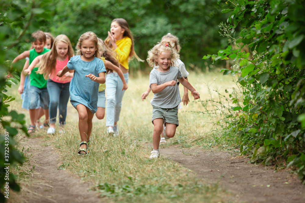 Happiness. Kids, children running on green forest. Cheerful and happy boys and girs playing, laughting, running through green blooming meadow. Childhood and summertime, sincere emotions concept.