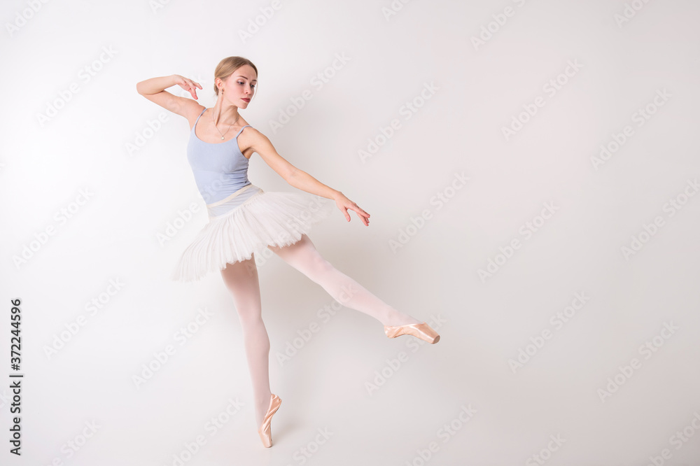 Young beautiful ballerina dances in big studio isolated on white background