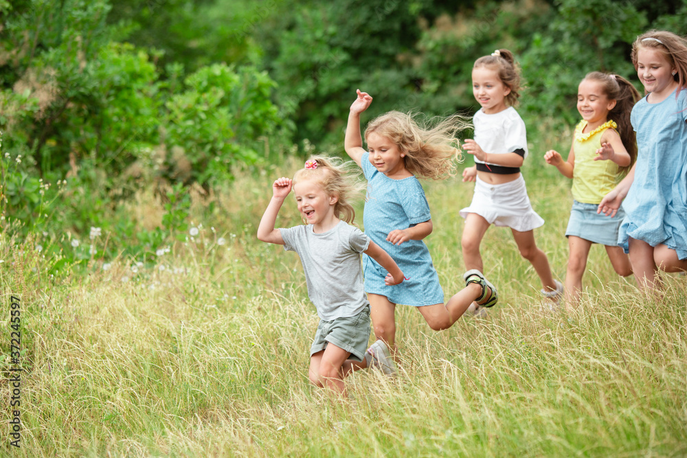 Angels. Kids, children running on green forest. Cheerful and happy boys and girs playing, laughting, running through green blooming meadow. Childhood and summertime, sincere emotions concept.