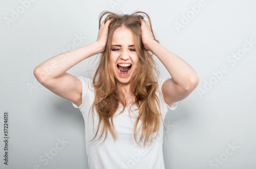 Angry young blong woman strong screaming with wide open mouth on light blue background. Closeup portrait © nastia1983