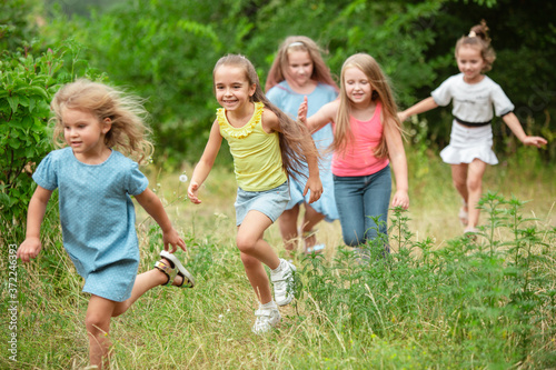 Angels. Kids, children running on green forest. Cheerful and happy boys and girs playing, laughting, running through green blooming meadow. Childhood and summertime, sincere emotions concept.