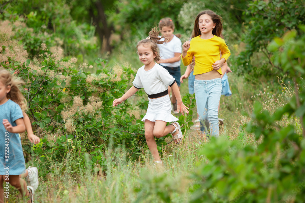 Obraz premium Best time. Kids, children running on green forest. Cheerful and happy boys and girs playing, laughting, running through green blooming meadow. Childhood and summertime, sincere emotions concept.