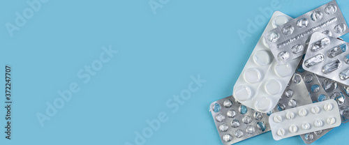 A pile Used blister packs of pills on blue background. Medical blisters packs opened and empty without pills top view. Medical wide banner with space for text.