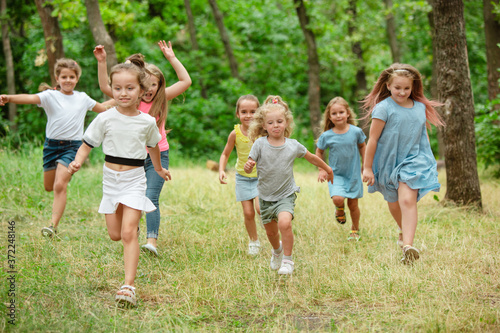 Memories. Kids, children running on green forest. Cheerful and happy boys and girs playing, laughting, running through green blooming meadow. Childhood and summertime, sincere emotions concept.
