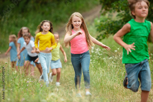 Summer. Kids, children running on green forest. Cheerful and happy boys and girs playing, laughting, running through green blooming meadow. Childhood and summertime, sincere emotions concept.