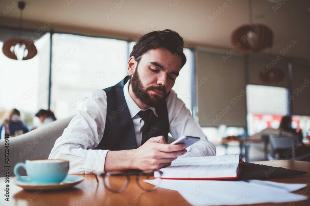 Bearded male blogger reading message from follover via telephone while creating new profile publication for social network, caucasian hipster guy updating notification on smartphone device indoors Bearded male blogger reading message from follover via telephone while creating new profile publication for social network, caucasian hipster guy updating notification on smartphone device indoors