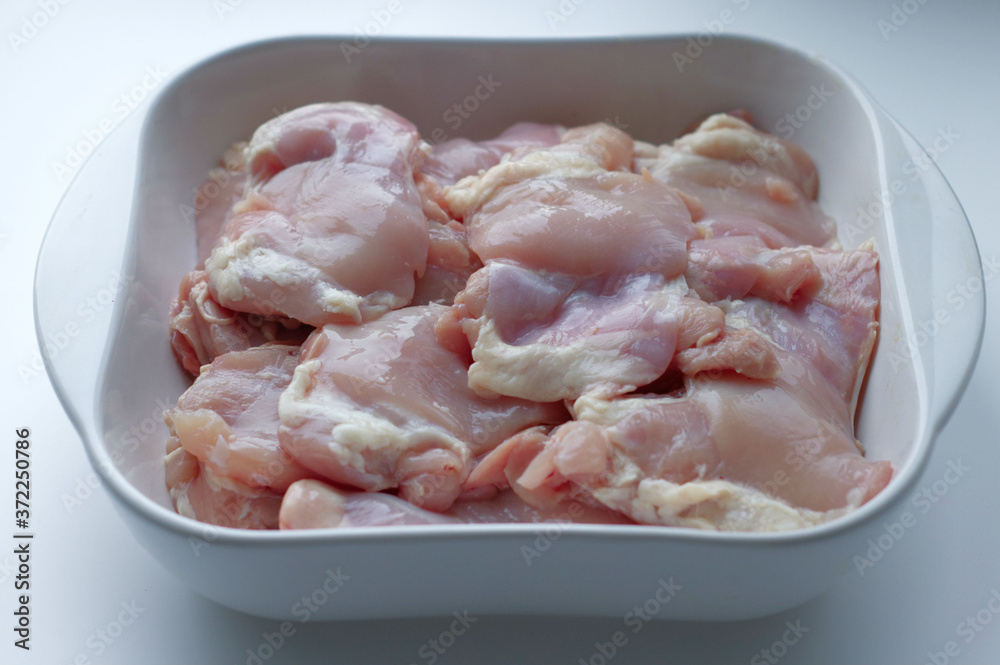 Chicken thigh fillet with skin, in a white glass plate, on a gray background. Ingredients, fresh, cut meat for cooking. Chicken parts, protein. Diet meat, fillet in a plate