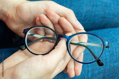 Close-up of human hands holding blue rimmed glasses on their knees. Eyes rest from glasses. Eye health concept