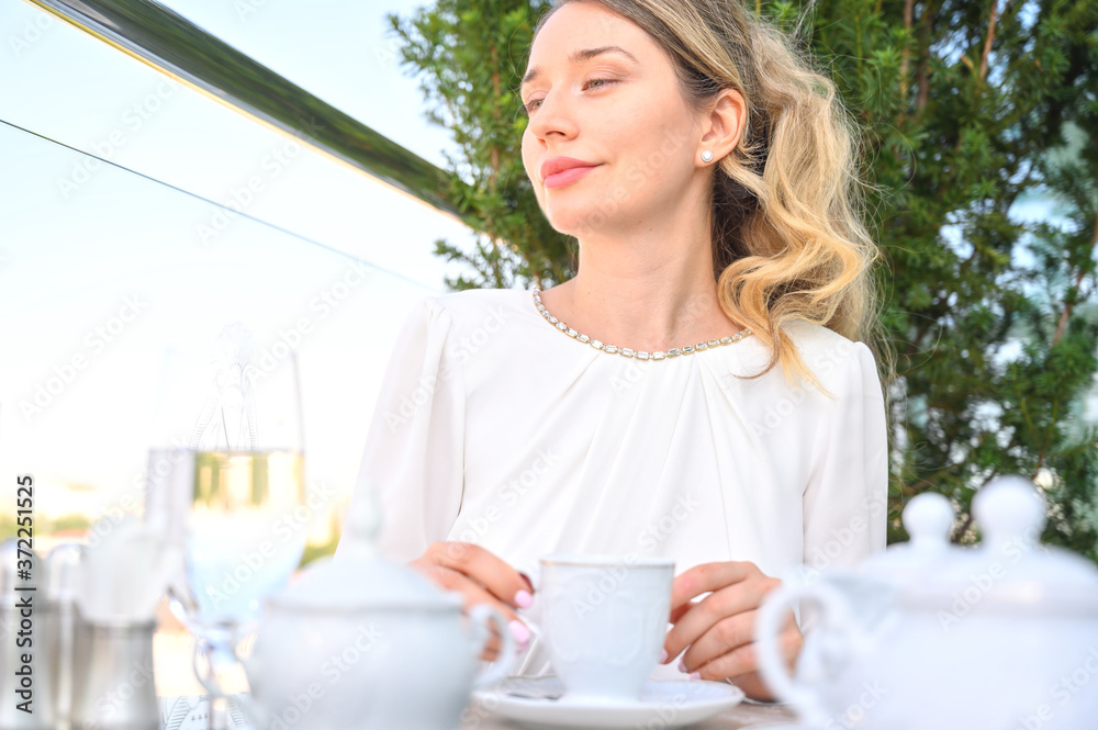 Woman drinking tea at a terrace and thinking about the future. Blonde girl White dress. Outdoors portraits Woman drinking tea at a terrace and thinking about the future. Blonde girl White dress. Outdoors portraits