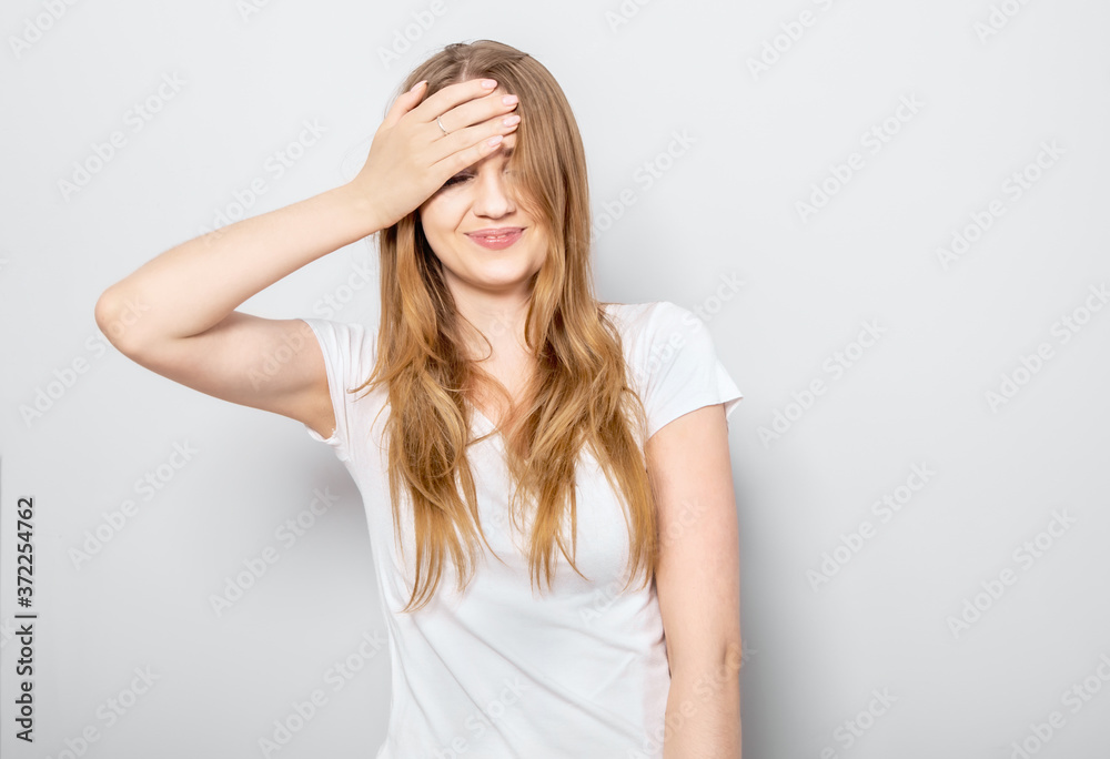 Laughing blond smiling student woman covering the face and hiding her eyes the hand on light blue background. Closeup portrait Laughing blond smiling student woman covering the face and hiding her eyes the hand on light blue background. Closeup portrait