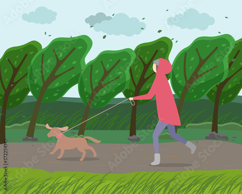 Walk with dog in the park. Woman is running with a doggy in garden strong windy weather. A happy pet walking with the owner against the backdrop of autumn landscape with a green trees bent to ground