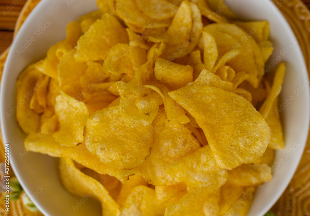 Crispy potato chips in bowl on wooden table, top view. Unhealthy eating concept. Close-up. Selective focus. Crispy potato chips in bowl on wooden table, top view. Unhealthy eating concept. Close-up. Selective focus.