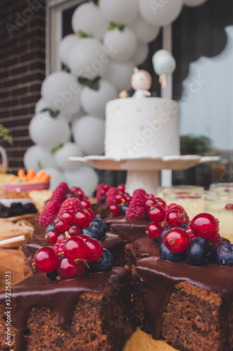 First anniversary party. Chocolate cake with berries on a wooden plate. Delicious desserts on rustic wooden table with the anniversary cake in the background. Diversity of pastry decorated with fruit.