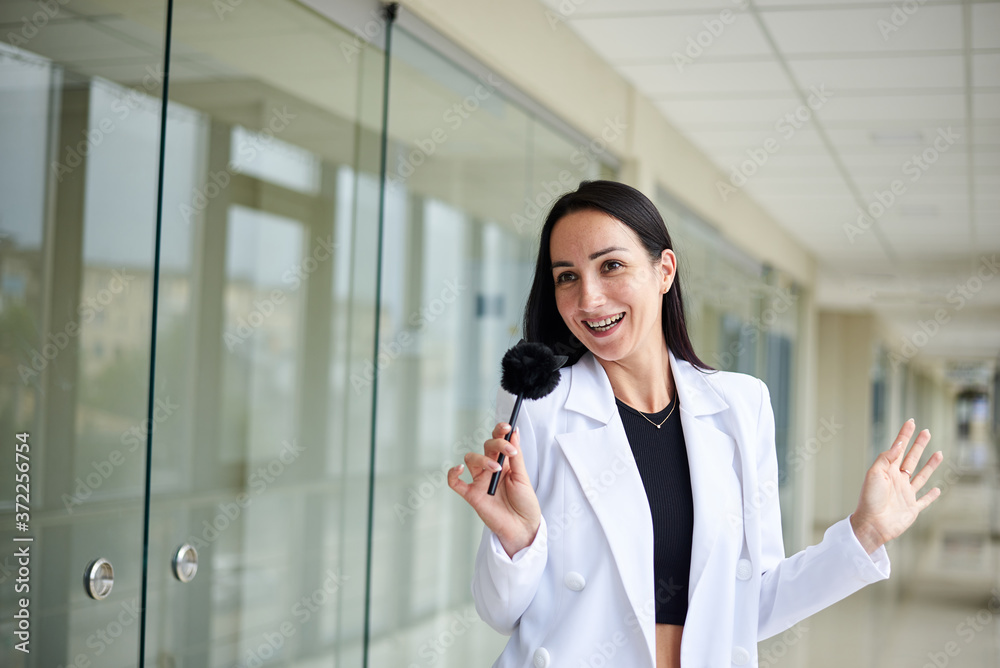 Young brunette woman, wearing white suit, holding cute fluffy pen with cat muzzle, standing in white office building. Businesswoman, getting ready for corporate meeting. Business relations concept.