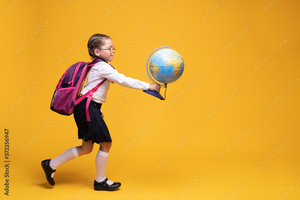a little girl in school uniform holds a globe in her hands on a yellow background