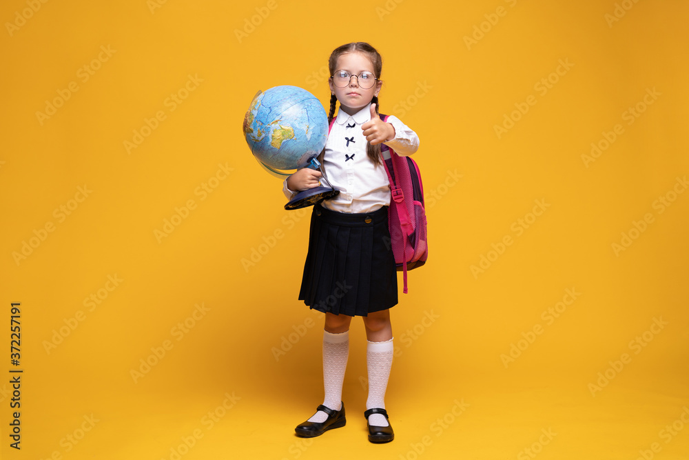 a little girl in school uniform holds a globe in her hands on a yellow background a little girl in school uniform holds a globe in her hands on a yellow background