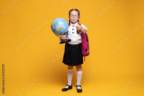 a little girl in school uniform holds a globe in her hands on a yellow background