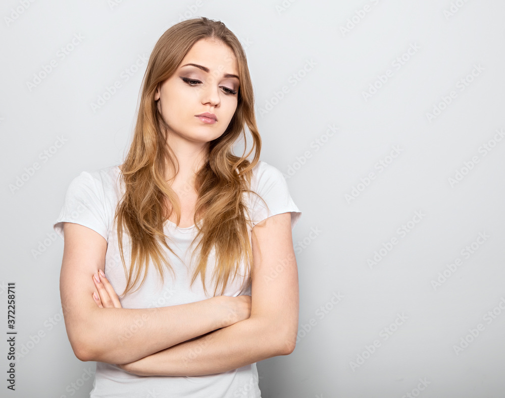 Thinking blond unhappy grimacing woman looking down and thinking with folded arms on light blue background. Closeup portrait with empty copy space. Thinking blond unhappy grimacing woman looking down and thinking with folded arms on light blue background. Closeup portrait with empty copy space.