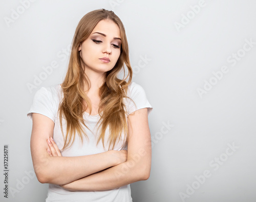 Thinking blond unhappy grimacing woman looking down and thinking with folded arms on light blue background. Closeup portrait with empty copy space.