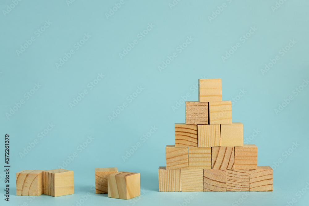 Fototapeta premium Construction of wooden cubes on blue background with copy space. Mockup composition for design