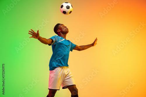 Leader. African-american male soccer, football player training in action isolated on gradient studio background in neon light. Concept of motion, action, ahievements, healthy lifestyle. Youth culture. © master1305